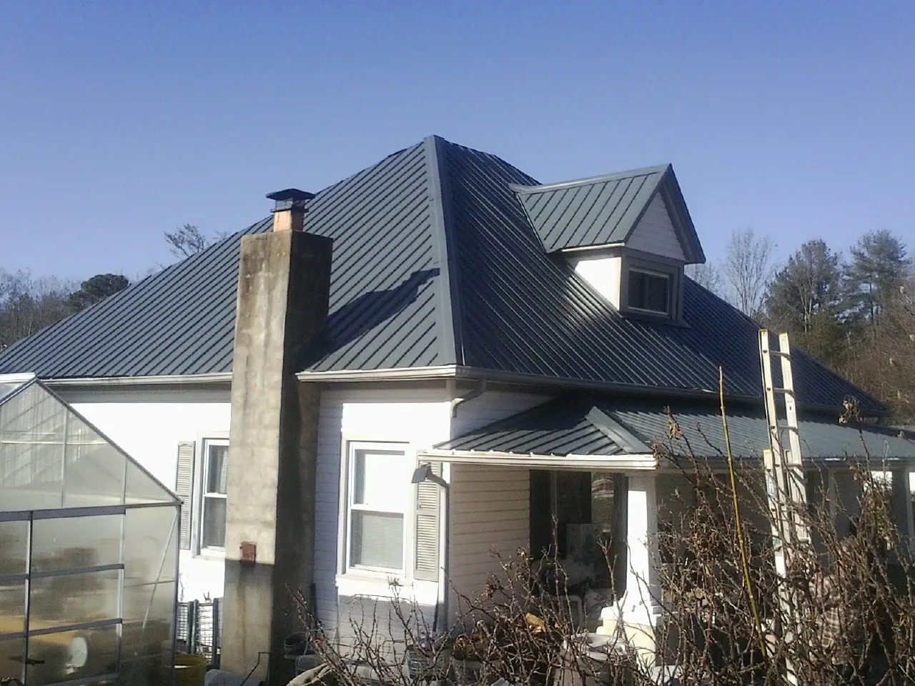 Dark blue standing seam metal roof on a white farmhouse with dormer — Slate & Tile Roof Repair by Roofing Brothers in Osterville