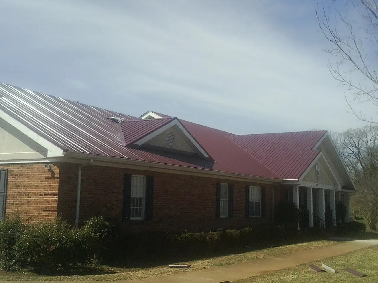 Red metal roof with gabled entries on a long brick building, from a Hail Damage Roof Repair job in Osterville