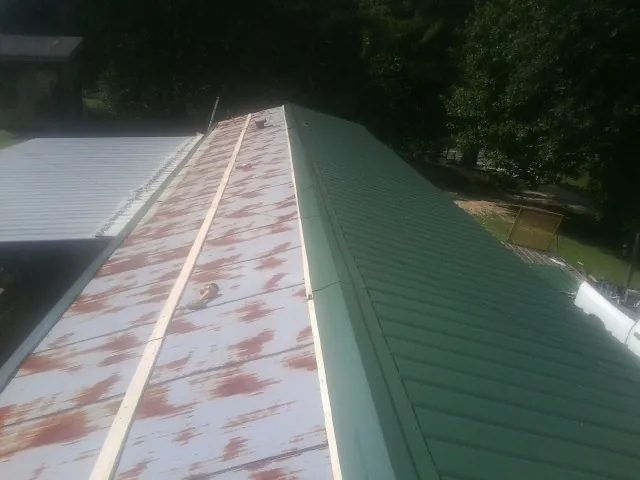 Old rusted panels beside newly installed green metal roofing — Wind Damage Roof Repair by Roofing Brothers in Osterville