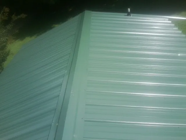 New green metal panels meeting at the ridge of a roof — Flat Roof Repair work by our crew in Osterville