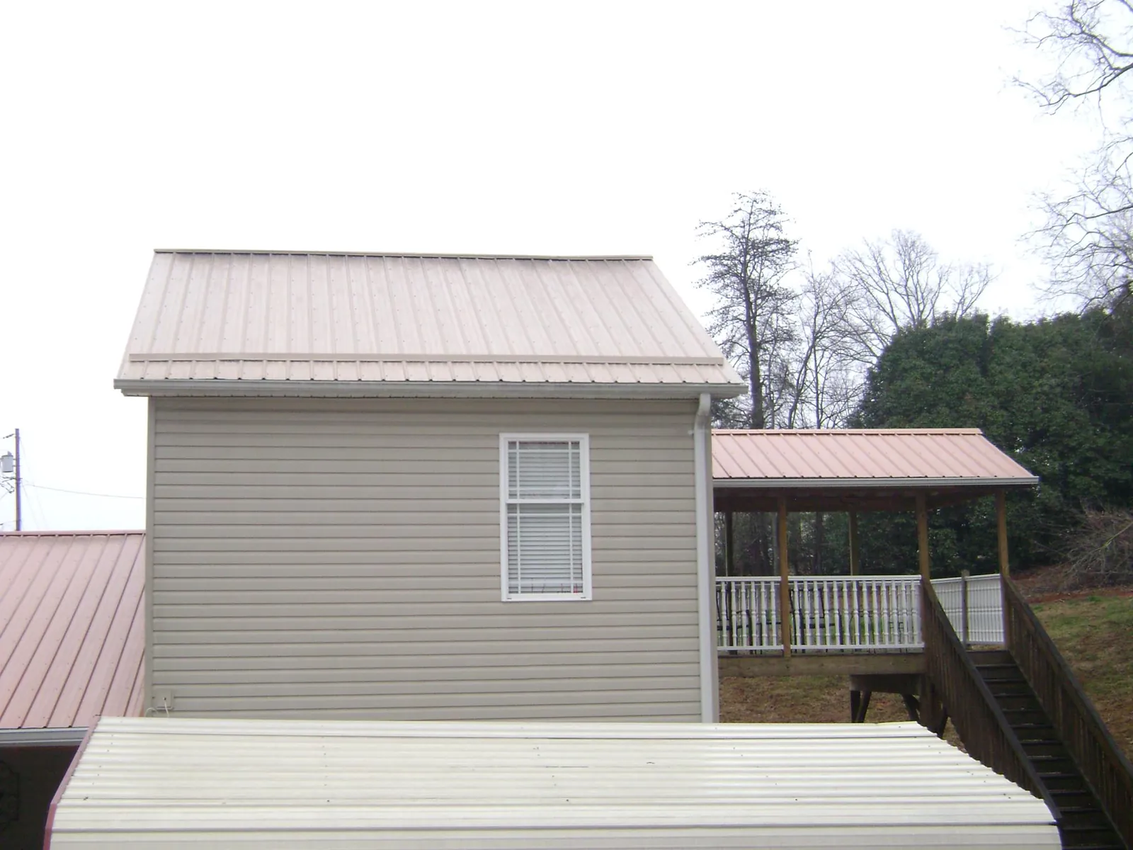 Tan metal roofs on a two story addition and attached porch, from a Roof Replacement job in Osterville
